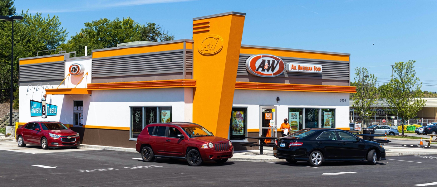 Exterior of A&W Restaurant in Richmond, Kentucky. Three cars are in the drive-thru. Team member is walking to a car holding an A&W to-go bag.